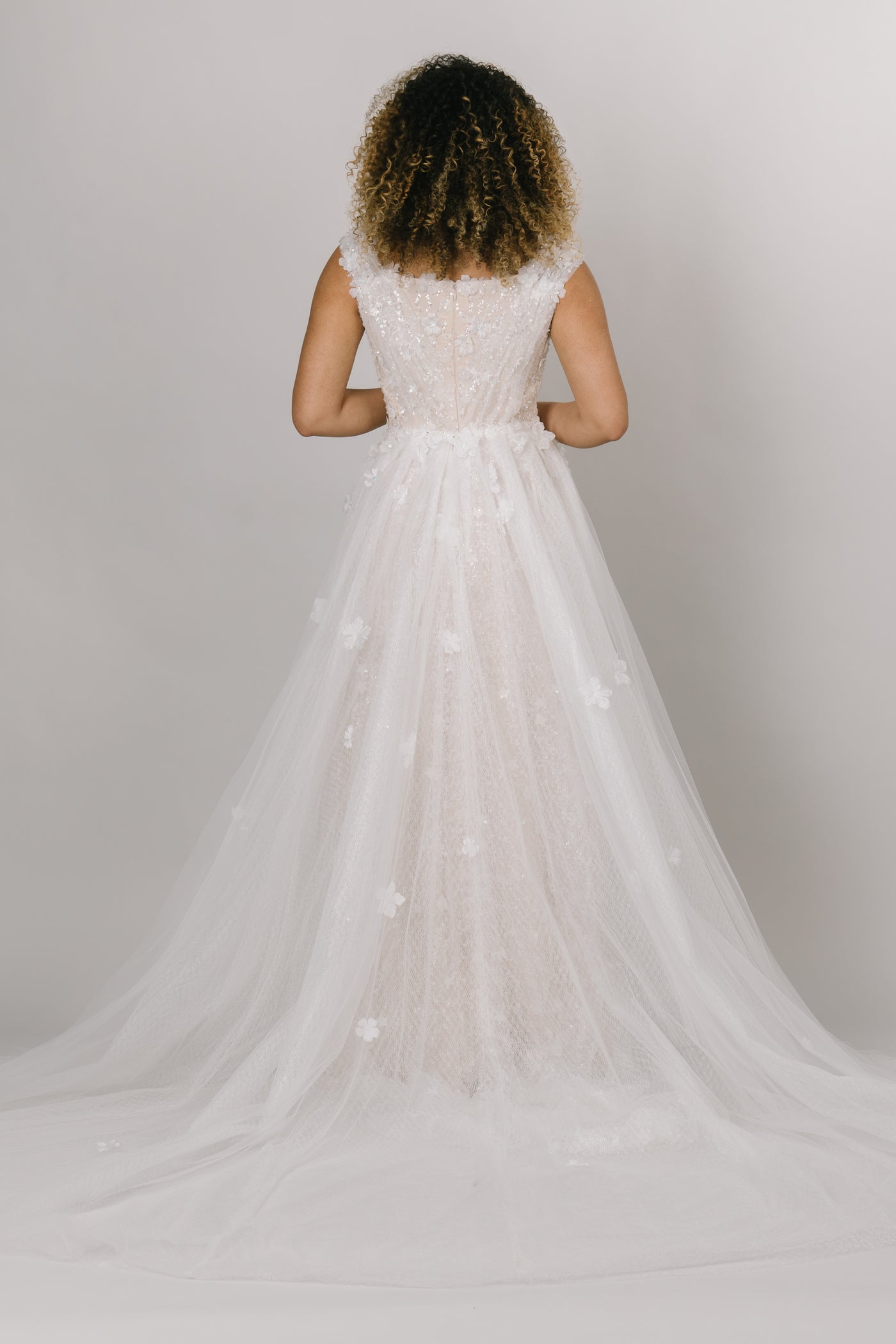 This gown did not miss a detail, featuring sequin detailing, floral and star appliques, and tulle rouching over the bodice., with an overskirt. The view is the back on the modest wedding dress.