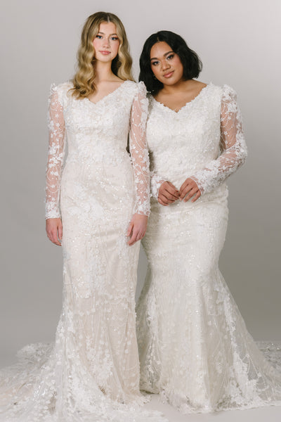Two models wearing the beautiful lace modest wedding dress by Moments Made Bridal. It has a v-neckline with a long lace sleeves. The sleeves have a slight puff at the top of the sleeve. It is a fitted fit with a long gorgeous train.