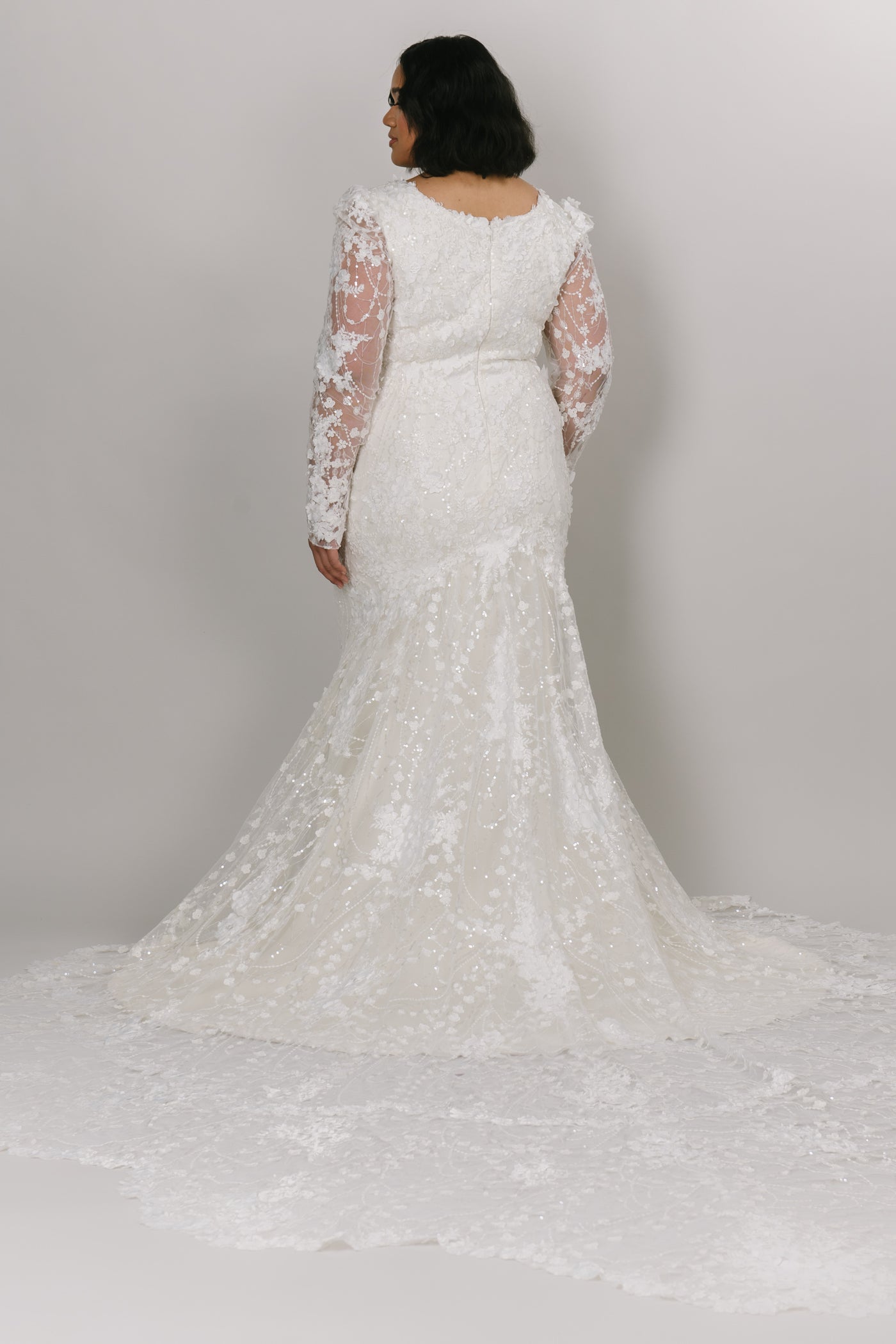 Back view of beautiful lace modest wedding dress by Moments Made Bridal. It has a v-neckline with a long lace sleeves. The sleeves have a slight puff at the top of the sleeve. It is a fitted fit with a long gorgeous train.