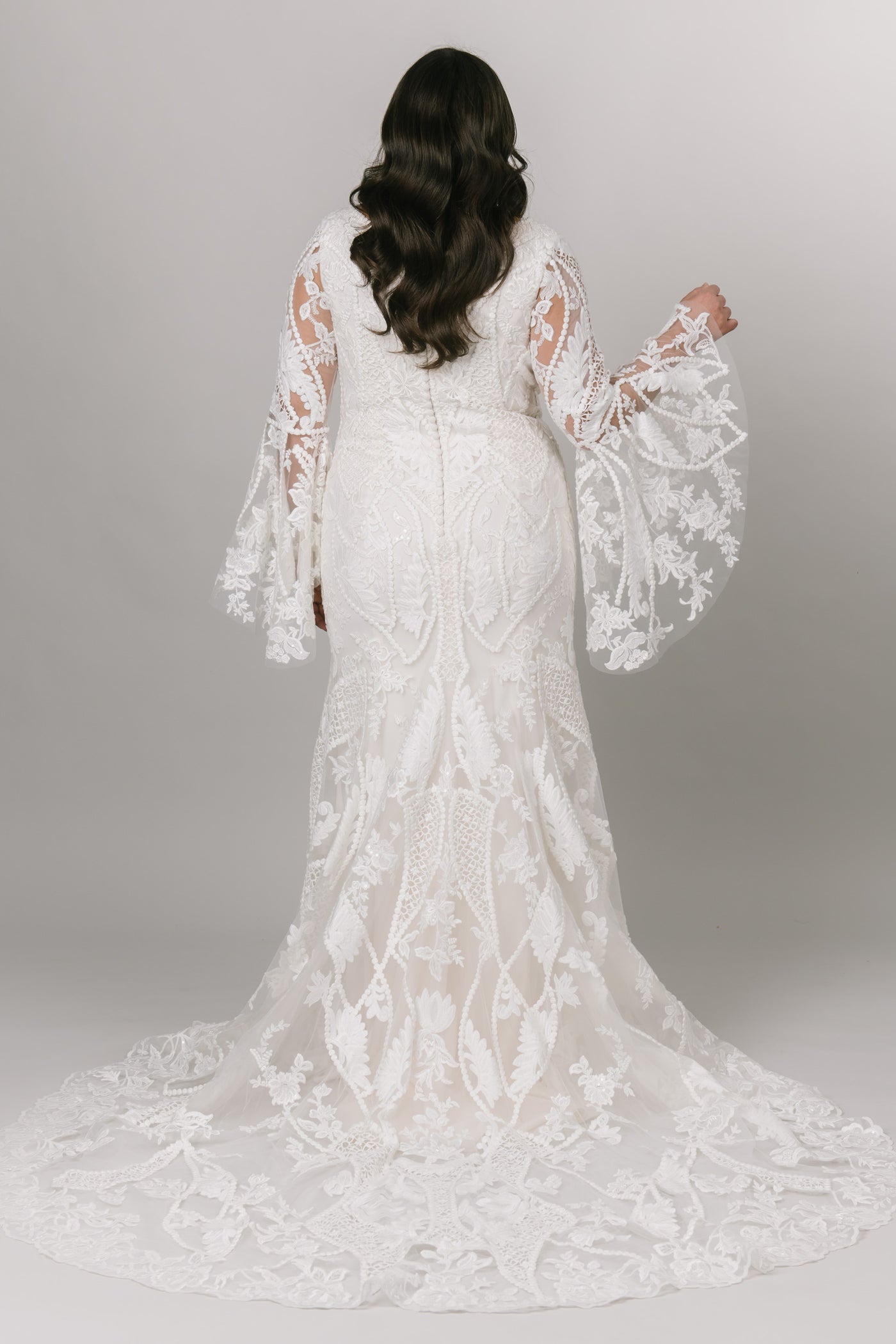 Back view of Moments Made Bridal boho styled wedding dress with long trumpet lace sleeves. It has a v-neckline and a fitted silhouette. Sheet lace covers the dress. This modest wedding dress is perfect for any wedding season.