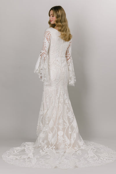 Back view of Moments Made Bridal boho styled wedding dress with long trumpet lace sleeves. It has a v-neckline and a fitted silhouette. Sheet lace covers the dress. This modest wedding dress is perfect for any wedding season.