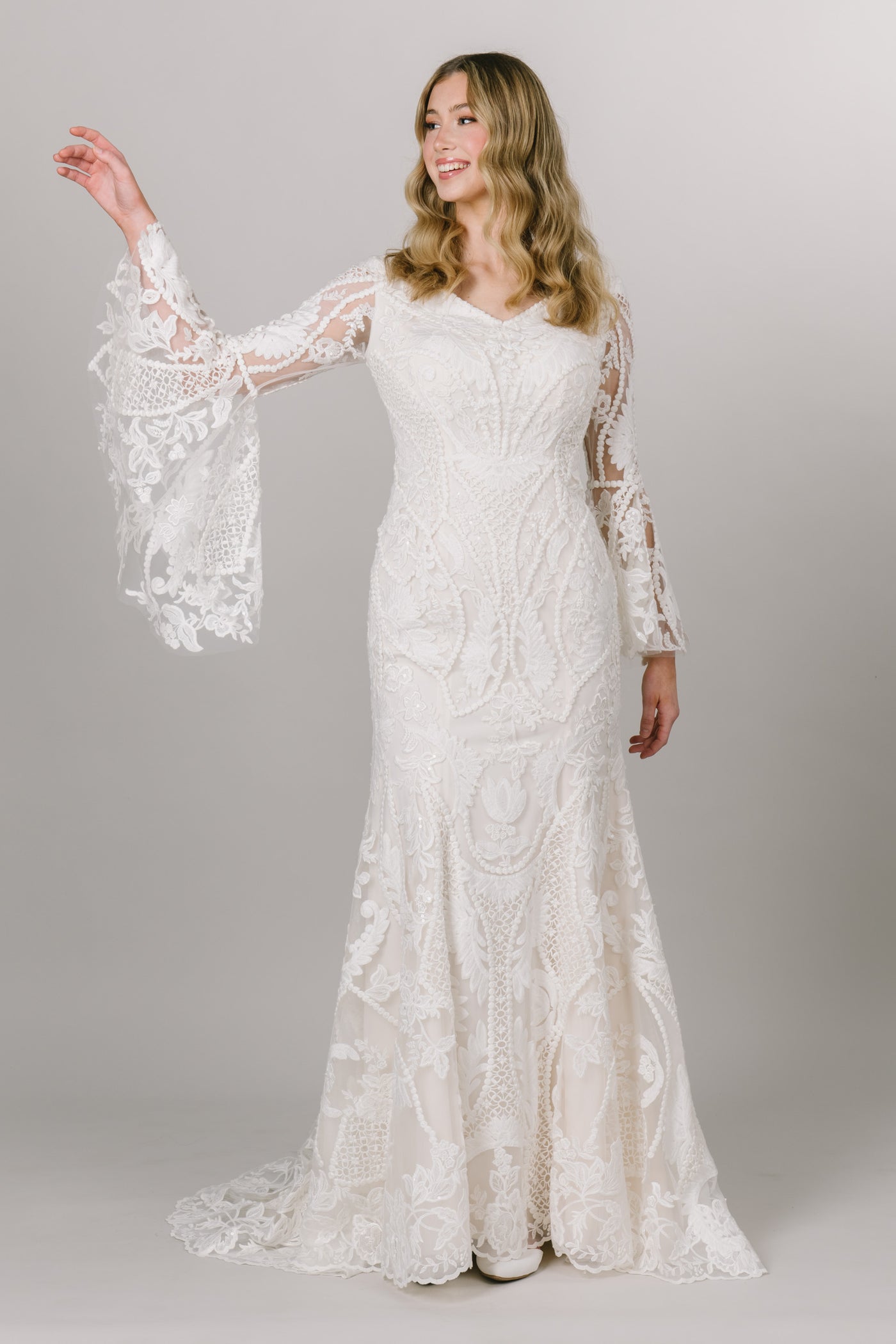 Moments Made Bridal boho styled wedding dress with long trumpet lace sleeves. It has a v-neckline and a fitted silhouette. Sheet lace covers the dress. This modest wedding dress is perfect for any wedding season. 