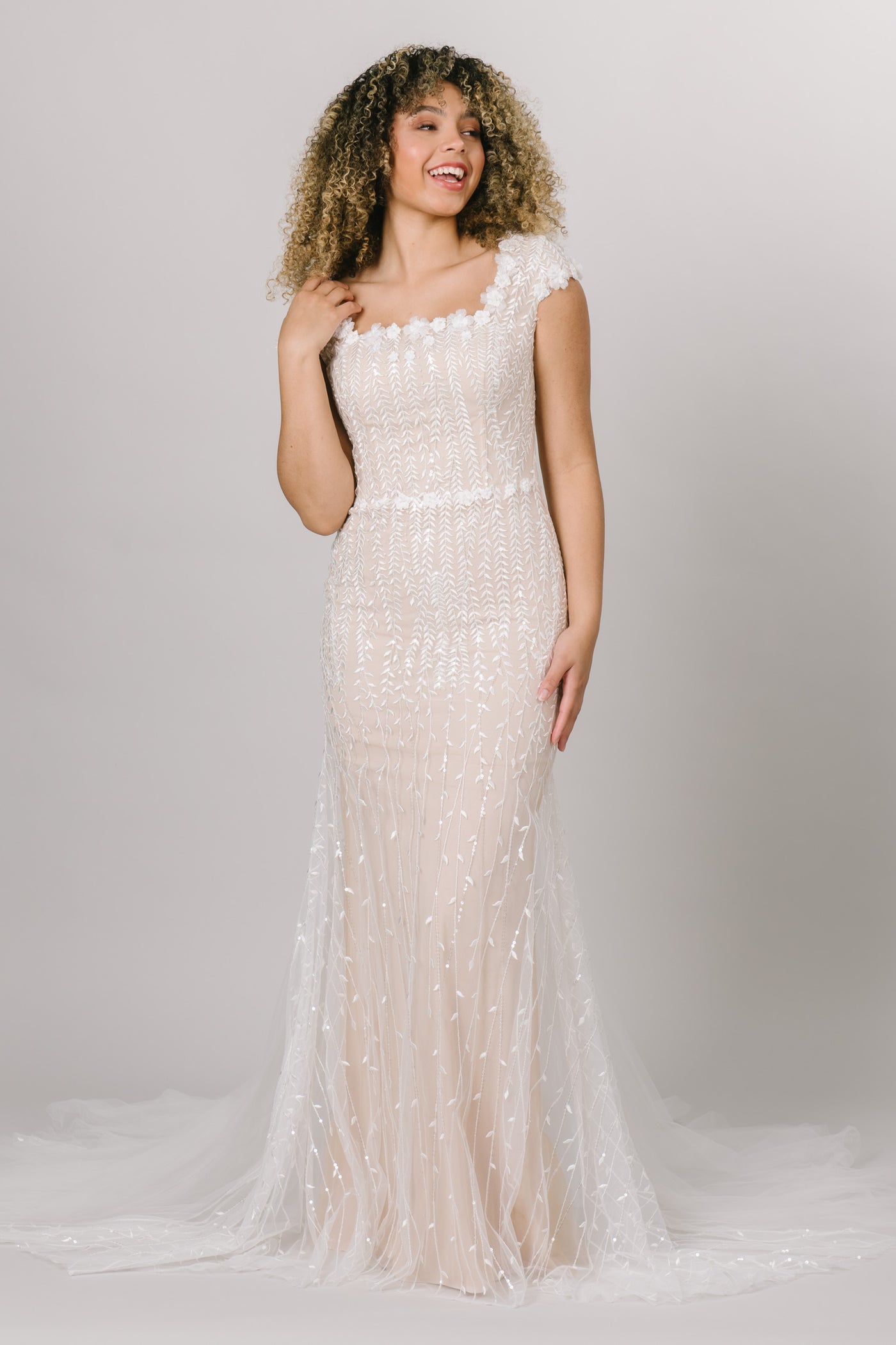 Front view of modest wedding dress, fitted silhouette with a square neckline. Champagne color underlining color with a delicate lace overtop.  