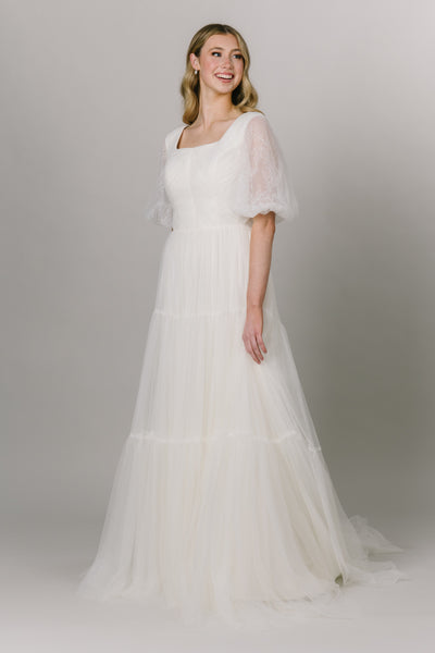Beautiful english tulle wedding dress. This modest wedding wedding is perfect any whimsical bride. It has stunning lace puffed sleeves and a square neckline. It's a-line fit and tiered skirt. 
