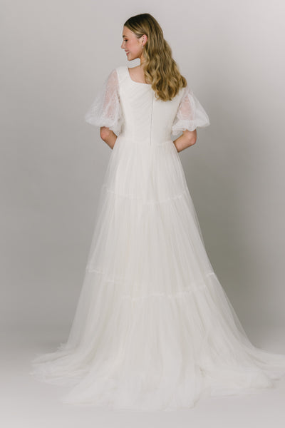 Back view of this beautiful english tulle wedding dress. This modest wedding wedding is perfect any whimsical bride. It has stunning lace puffed sleeves and a square neckline. It's a-line fit and tiered skirt.