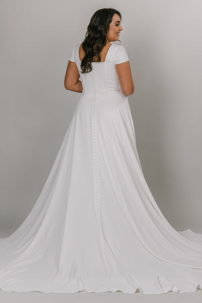 Plus size model wearing modest wedding dress that is a-line with a square neckline. It has a more constructed top with cap sleeves.