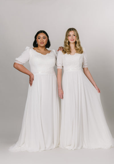Two models wearing the same modest wedding dress with a-line silhouette and v-neckline. The bottom is made with chiffon fabric and the top is has delicate lace with puffed sleeves.