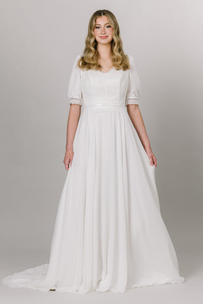 Front view of modest wedding dress with a-line silhouette and v-neckline. The bottom is made with chiffon fabric and the top is has delicate lace with puffed sleeves.