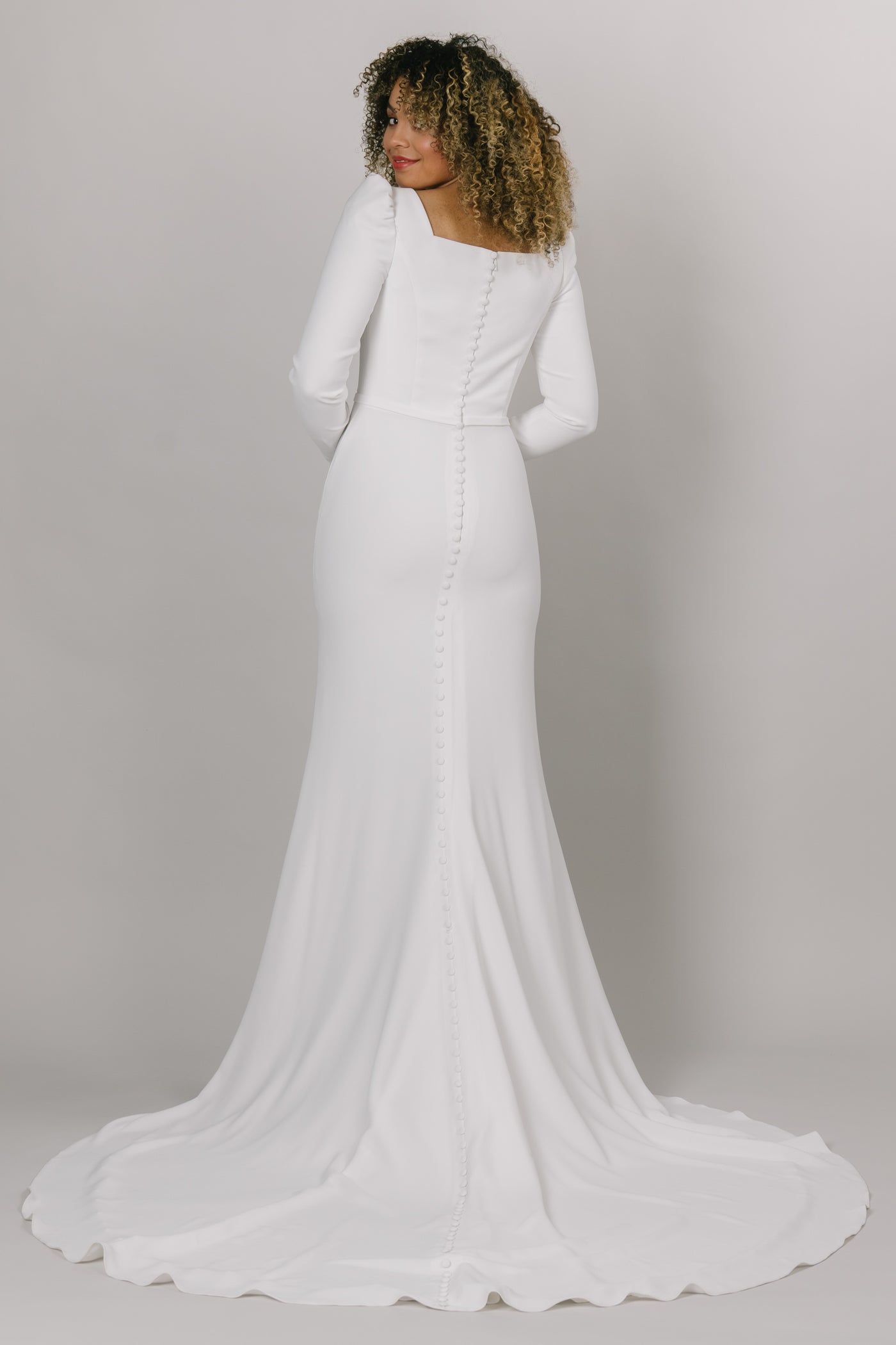 Back view of modest wedding dress with long puffed sleeves. This dress is fitted with a knee high slit and a square neck line. 