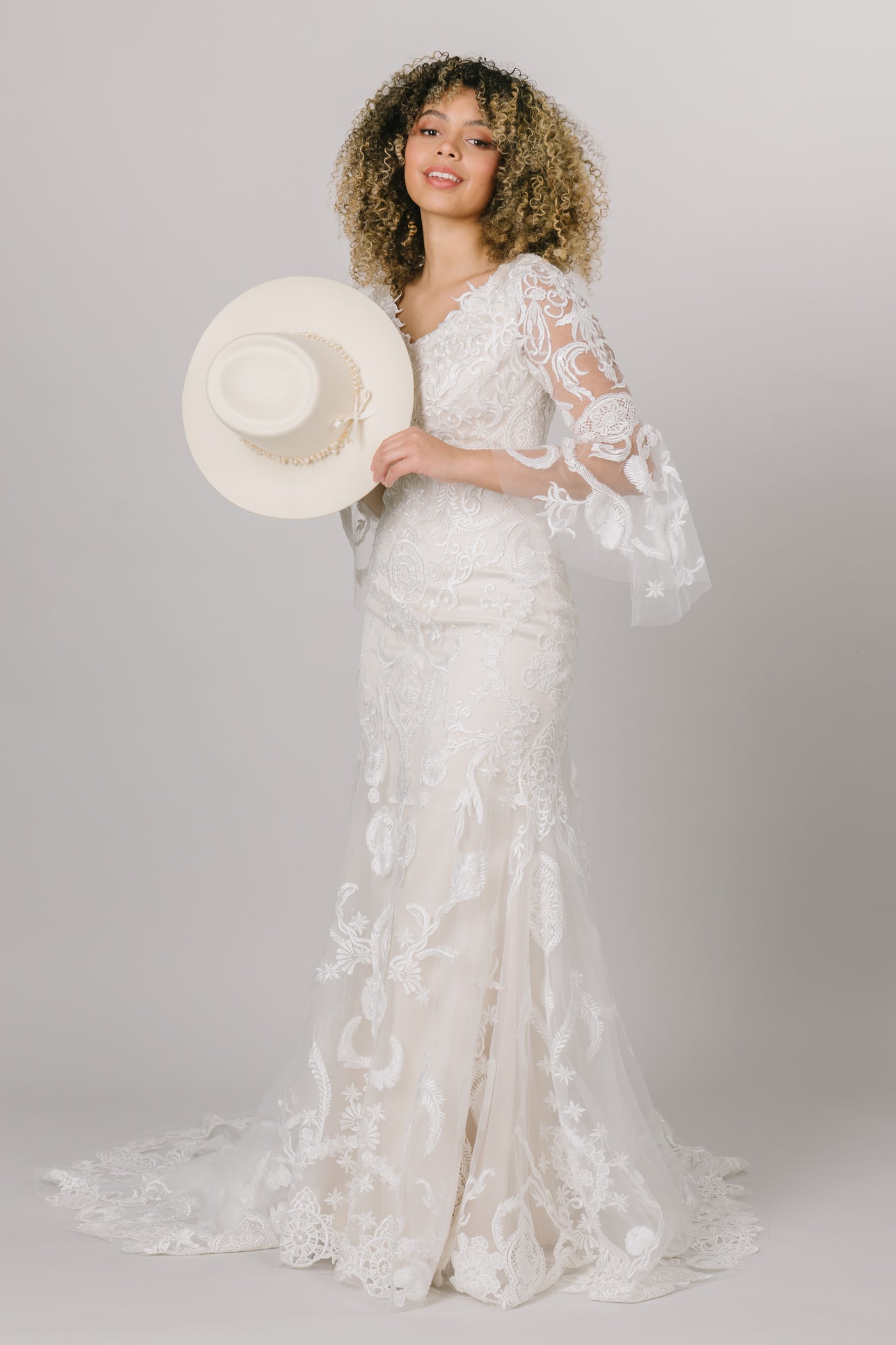 This modest wedding dress has a lace pattern and complemented with beautiful bell sleeves with a cream hat and in an ivory color.