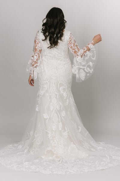 Back  view of a modest wedding dress features a stunning lace pattern over a fitted silhouette.