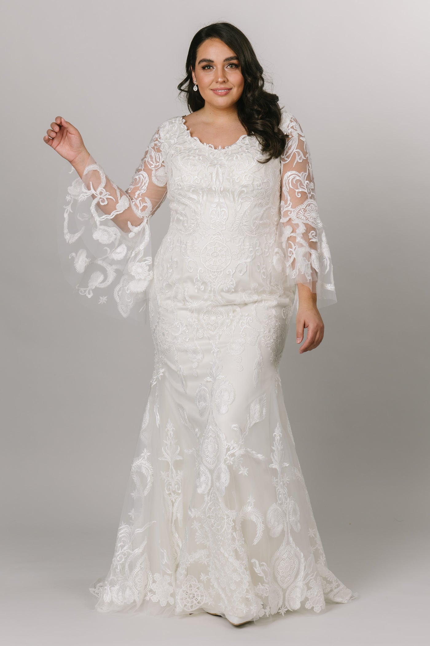Front view of a modest wedding dress features a stunning lace pattern over a fitted silhouette.