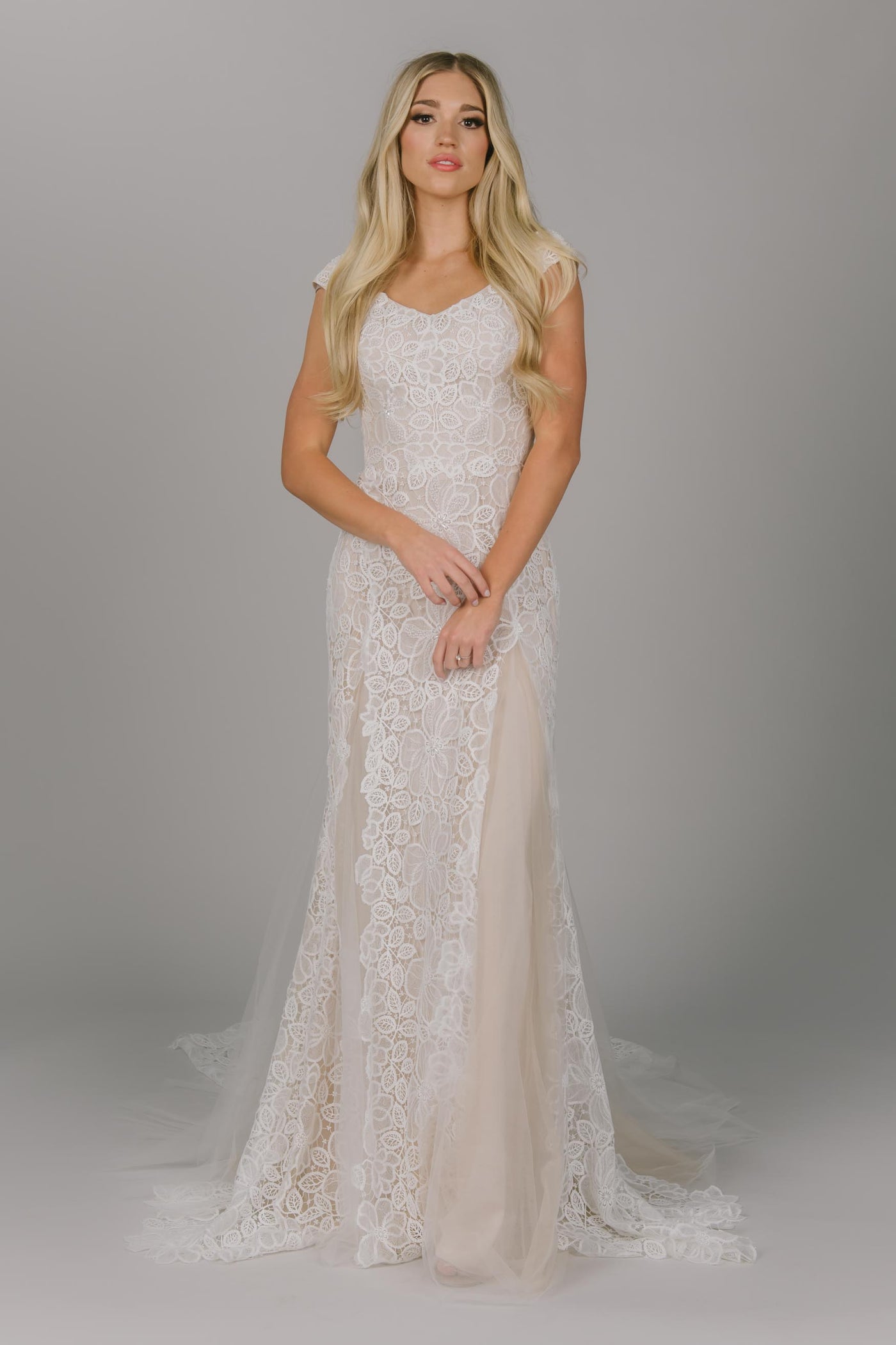 Fitted modest wedding dress featuring flower petal lace. It has a v-neckline and champagne underlay. It has cap sleeves and tulle slits. Absolutely stunning for any modest wedding dress bride.  