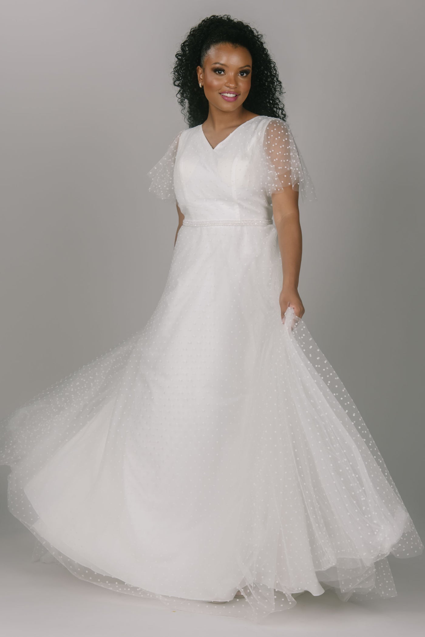 Party modest wedding dress with swiss dots. This dress has flutter sleeves and a sparkly thin belt. This v-neckline dress is the perfect modest wedding dress.