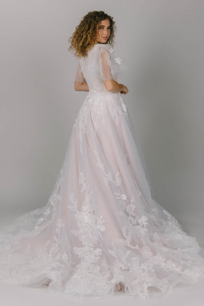 Back view of modest wedding ballgown. It has large tulle flutter sleeves. Beautiful flower lace covers the dress. It has a v-neckline and a train.
