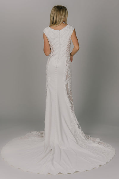 Back view of boho style modest wedding dress. It has larger soft lace on the sides of the dresses. It has a v-neckline and has a fitted fit. It is cap sleeved but easy to move in. It has buttons all the way down the back. 
