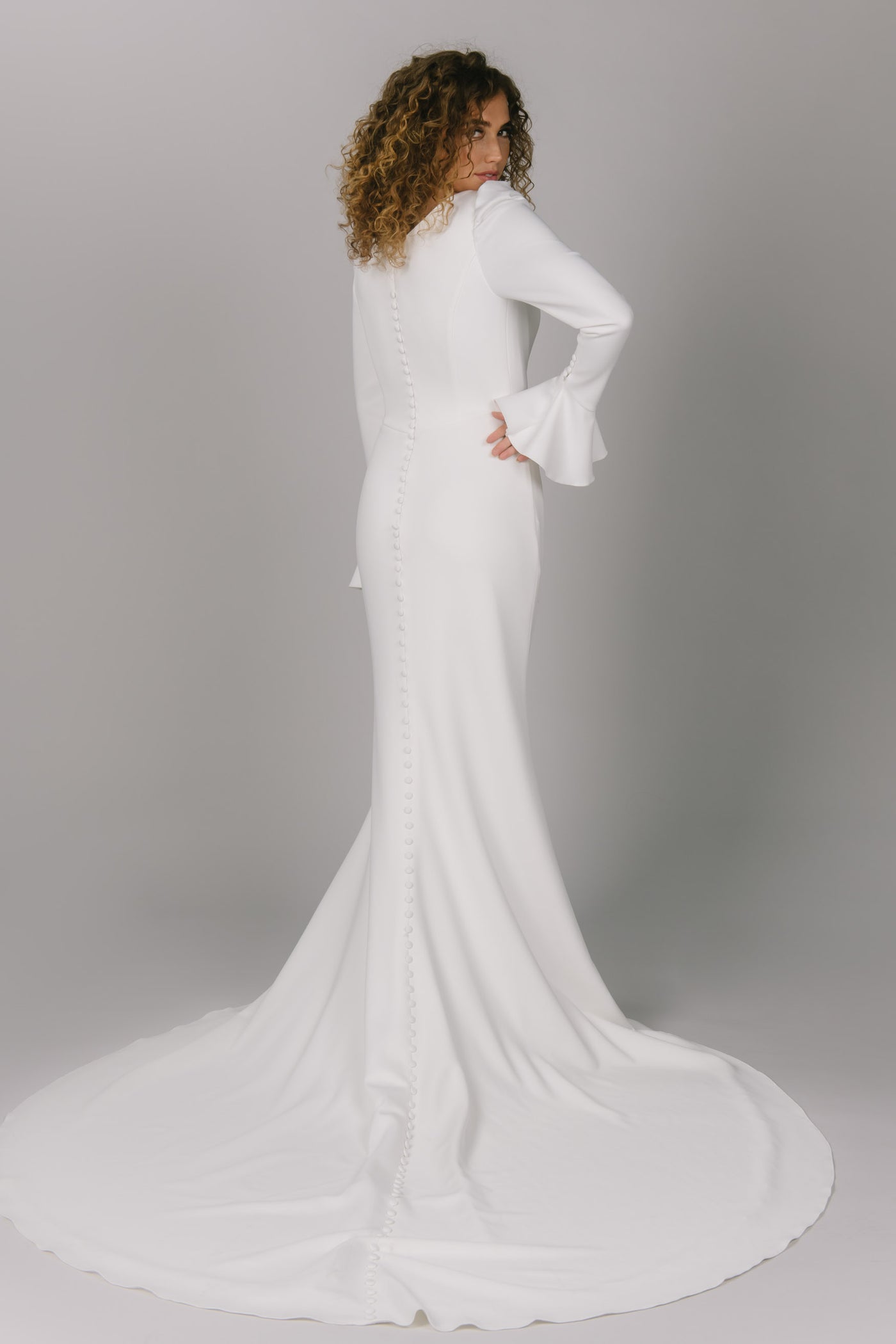 Back view of modest wedding dress with long trumpet-styled sleeves. This dress has a v-neckline and slit in the skirt. It does have a longer train to add drama. It has beautiful buttons all the way down the train. Timeless modest wedding dress.
