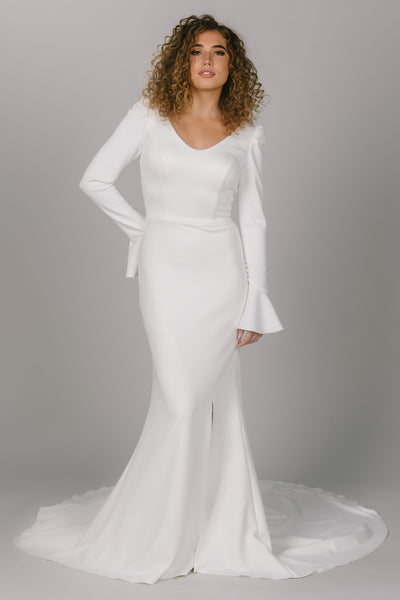 Front view of modest wedding dress with long trumpet-styled sleeves. This dress has a v-neckline and slit in the skirt. It does have a longer train to add drama. Timeless modest wedding dress.